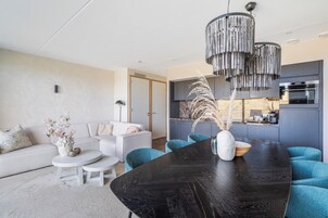 A modern living room with a black dining table, white sofas, and teal chairs.
