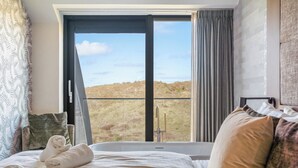 Habitación de hotel con una cama grande, vista a un paisaje cubierto de hierba a través de un ventanal corredero y una ventana con cortinas.