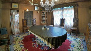 A room with a round table, chairs, a chandelier, ceiling fans, and patterned curtains. - Chicago Houseboats  (Srinagar)
