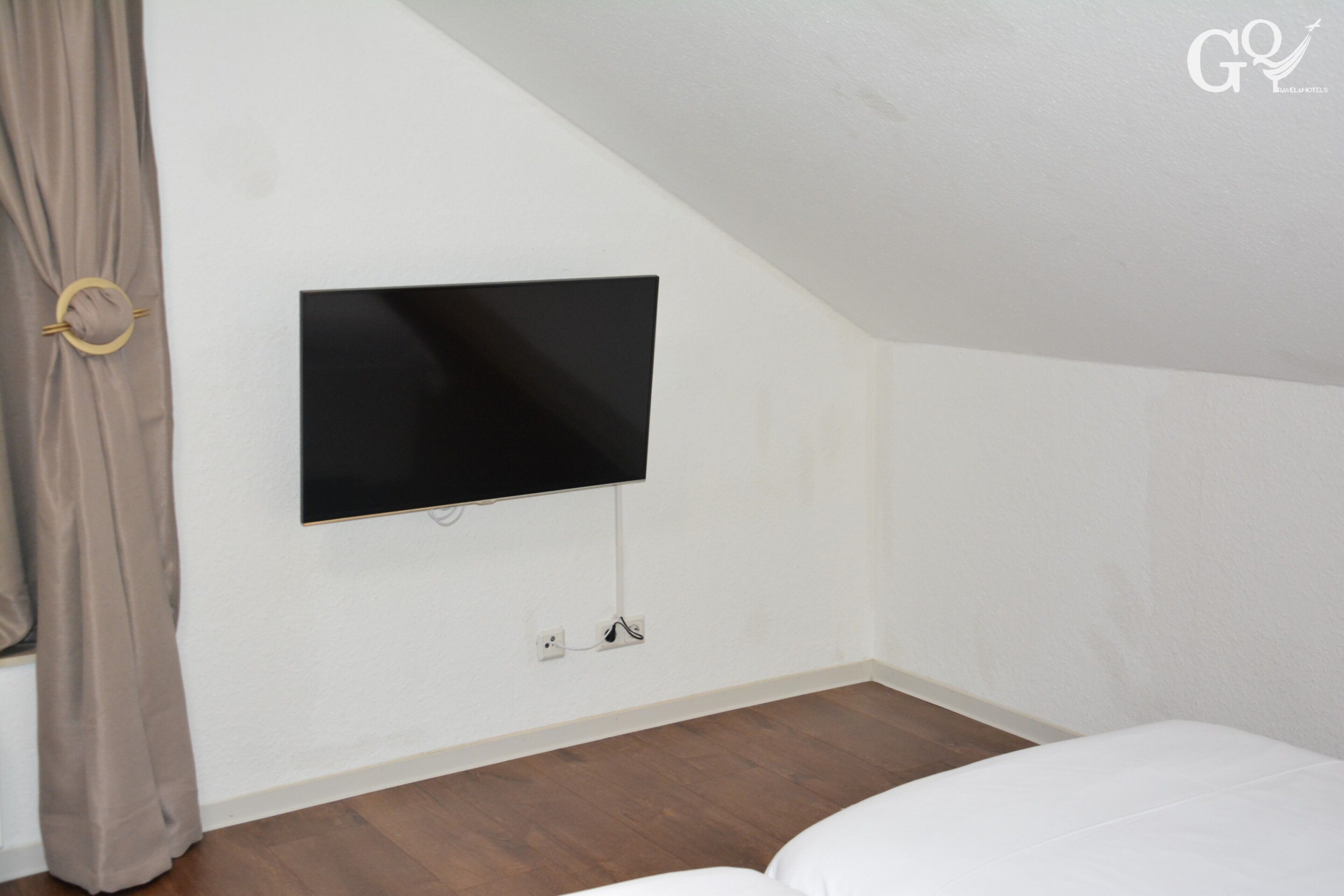 Ein Schlafzimmer mit Flachbildfernseher an der Wand, einem Fenster mit Vorhängen und Holzboden.
