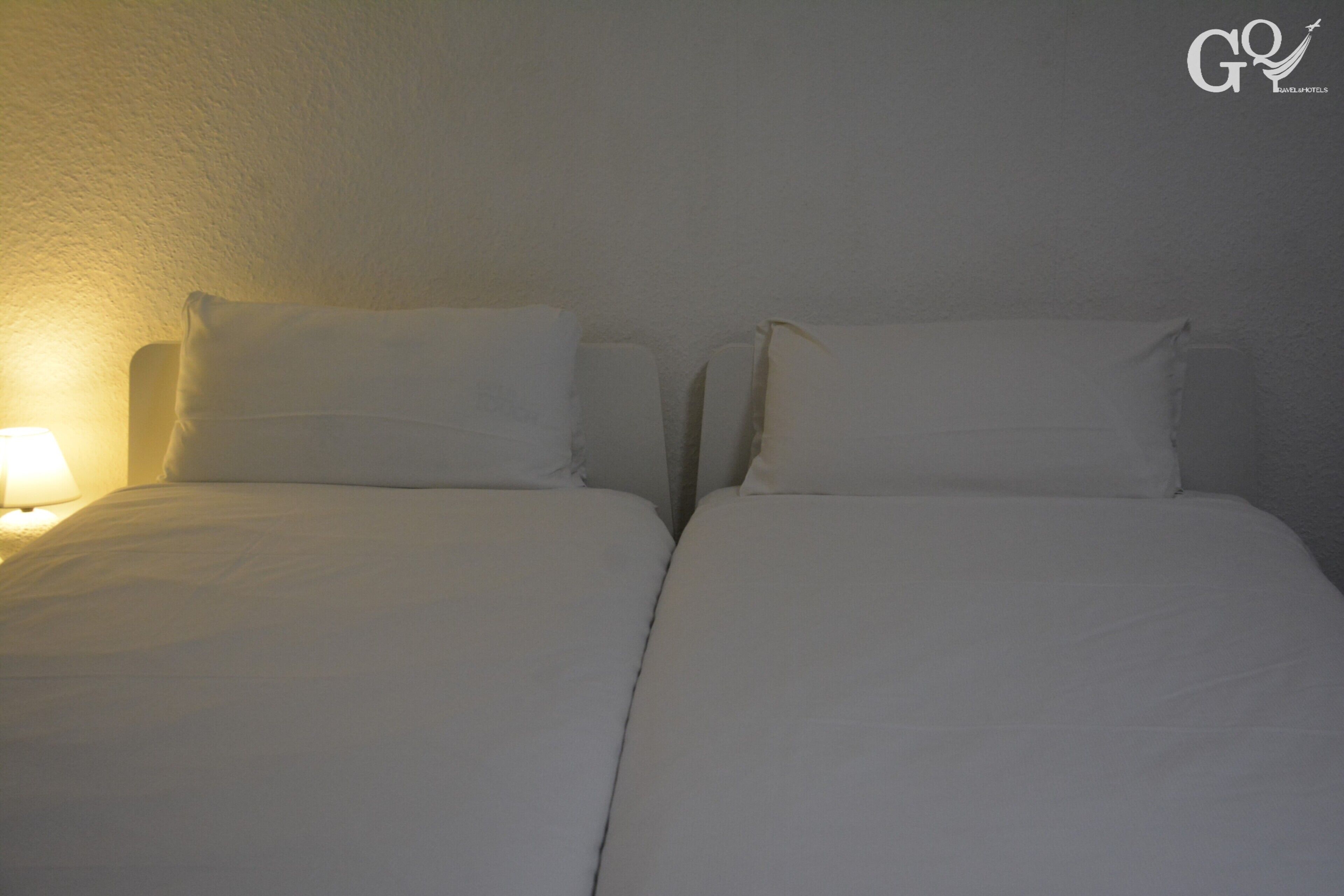 Een sober bed met witte lakens en een enkele bedlamp.