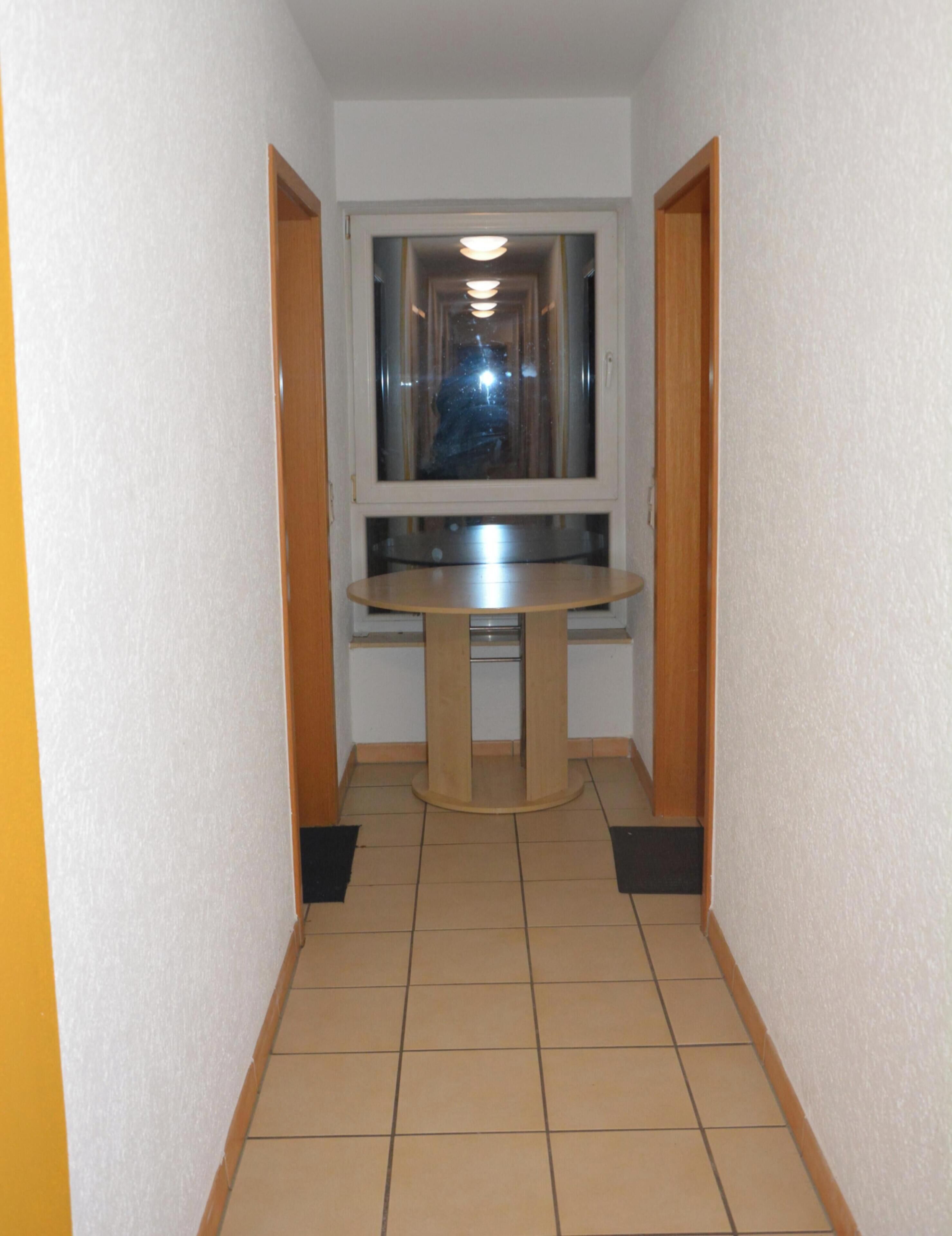 A narrow hallway with a round table in the center, flanked by two wooden doors.