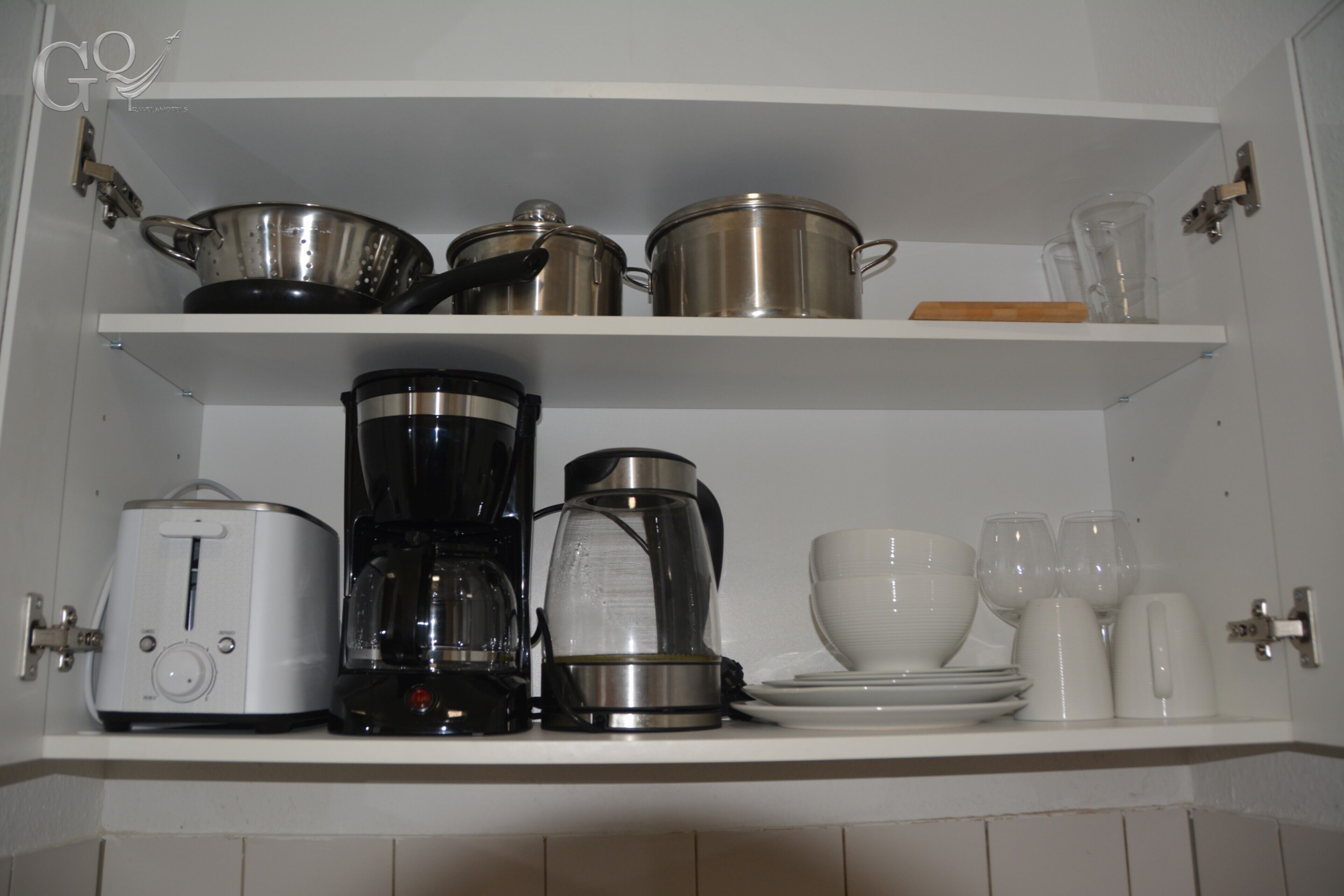 Een keuken met witte kastjes, een broodrooster, een koffiezetapparaat, pannen, kommen en glazen.