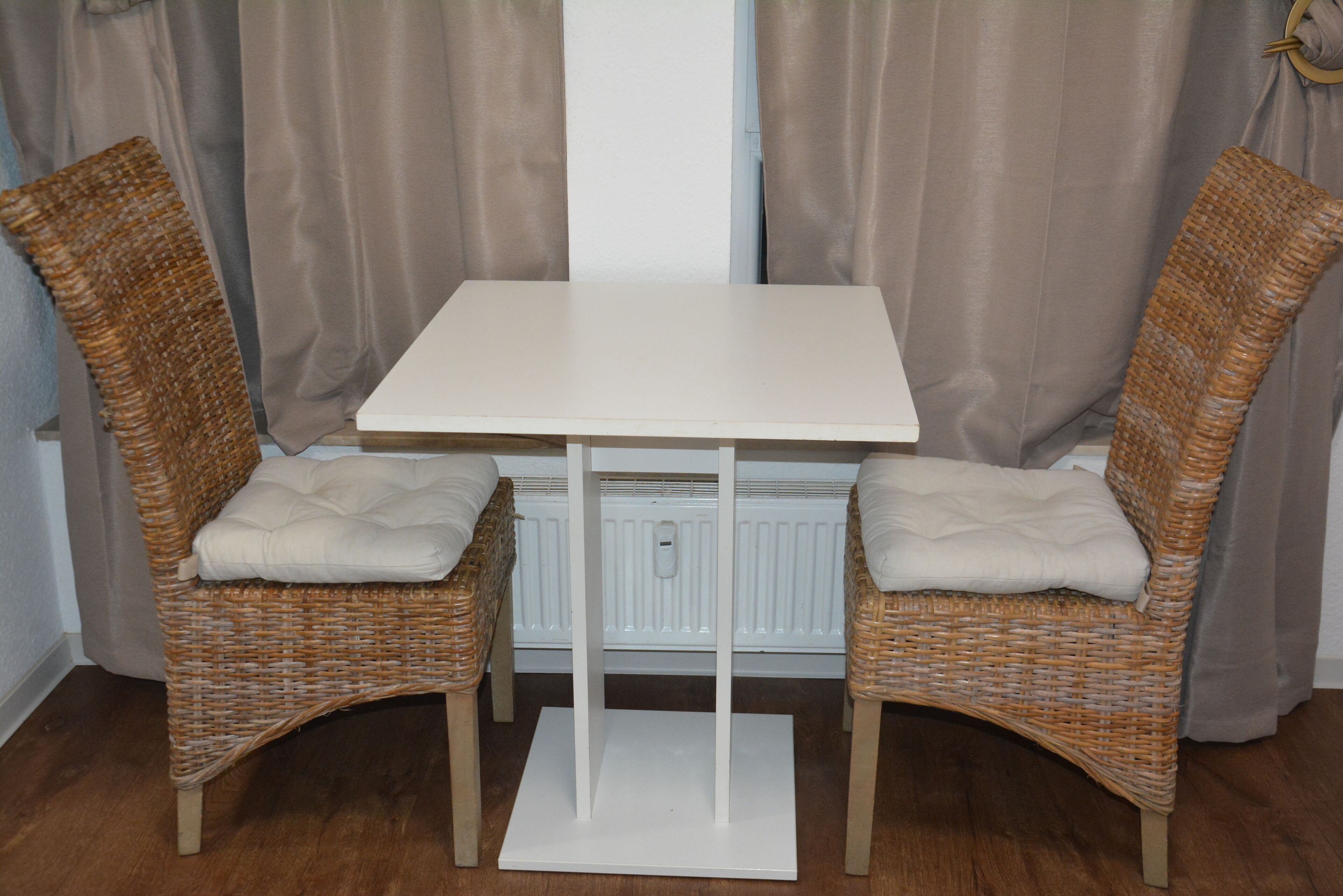 Une table blanche, accompagnée de deux chaises en osier, chacune dotée d’un siège et d’un dossier rembourrés.