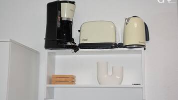 A white shelf with a coffee maker, a toaster, and a kettle.