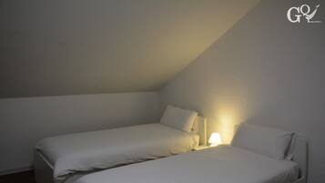 A small, dimly lit room with two single beds, a nightstand with a lamp, and a sloped ceiling.