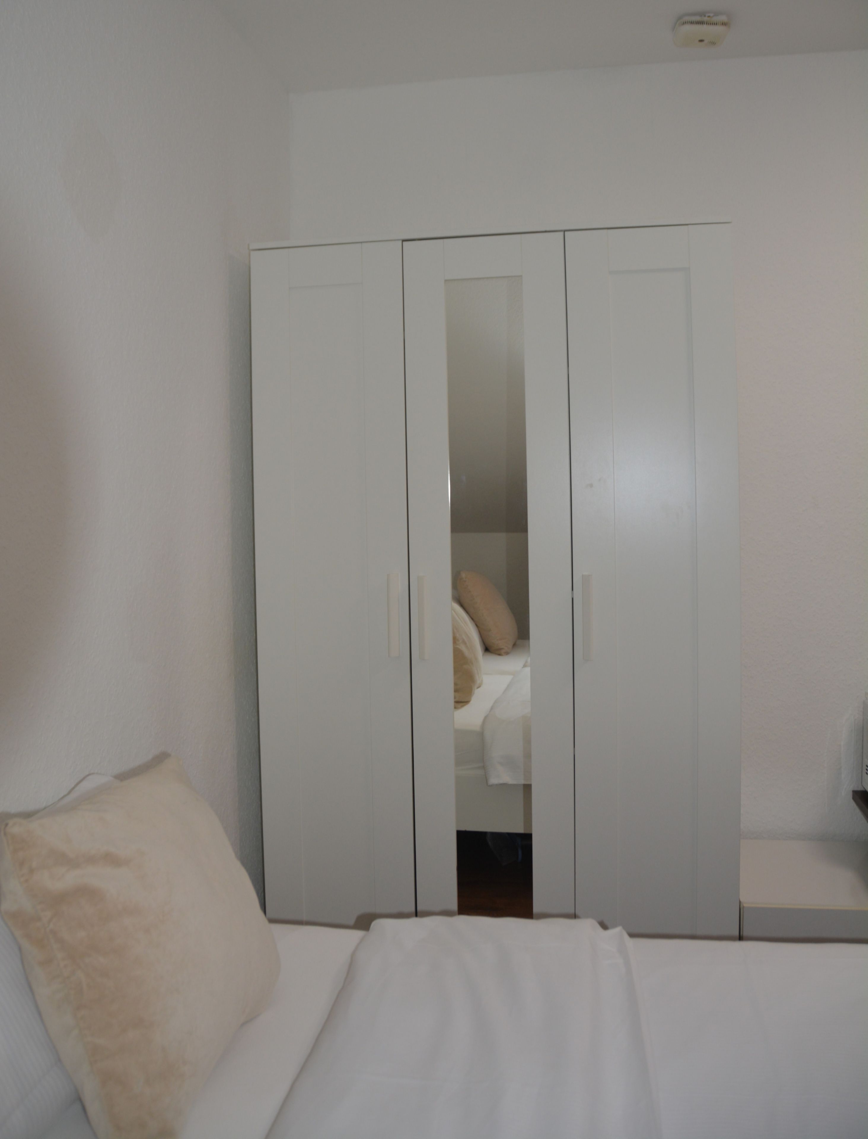 A bedroom with a bed, a white wardrobe, and a bedside table.