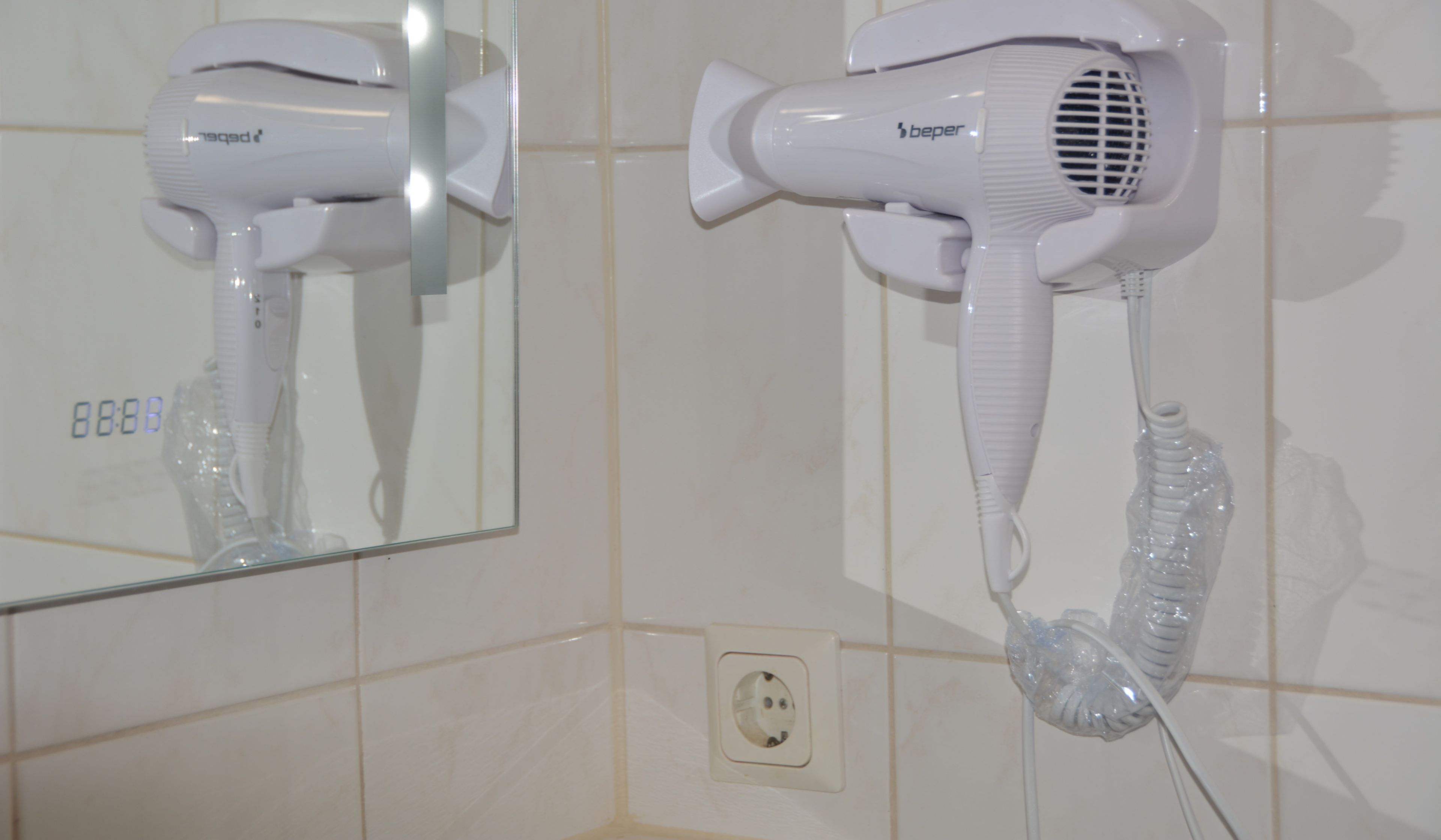 Two white hair dryers mounted on a wall with a mirror reflection.