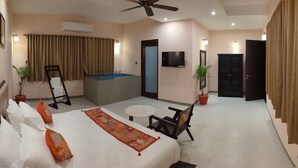 Une chambre d’hôtel avec un lit, une petite table, une chaise, un ventilateur de plafond, une télévision, une porte et une baignoire.