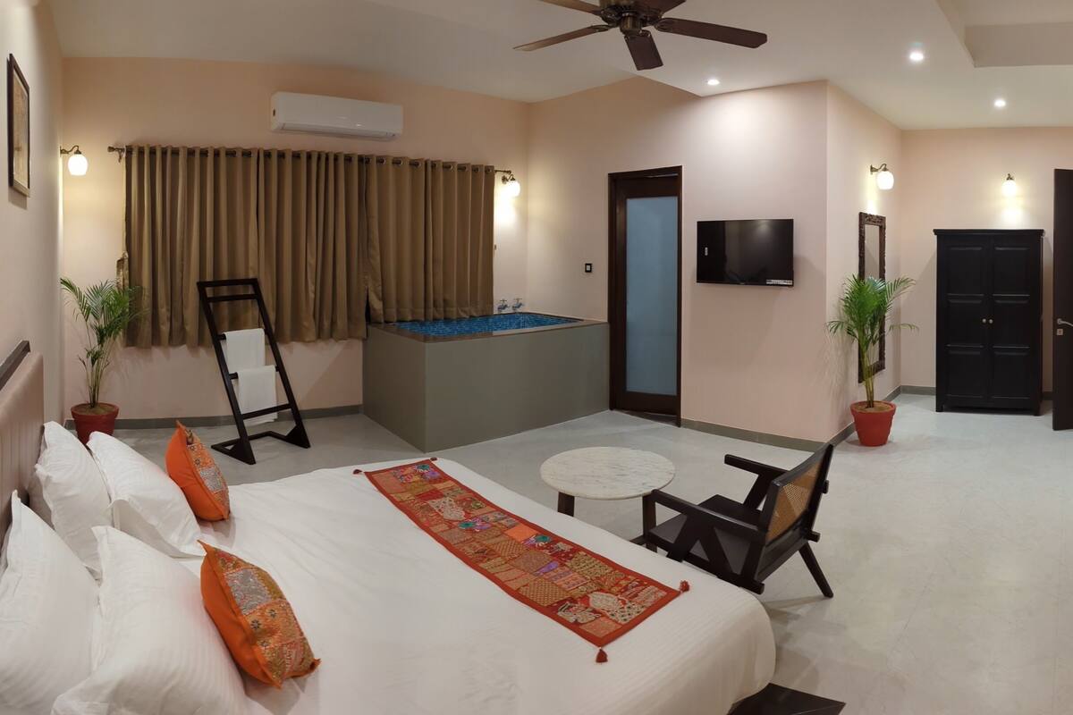 A hotel room with a bed, a small table, a chair, a ceiling fan, a TV, a door, and a bathtub.