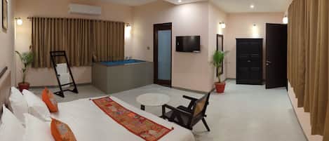 A hotel room with a bed, a small table, a chair, a ceiling fan, a TV, a door, and a bathtub.