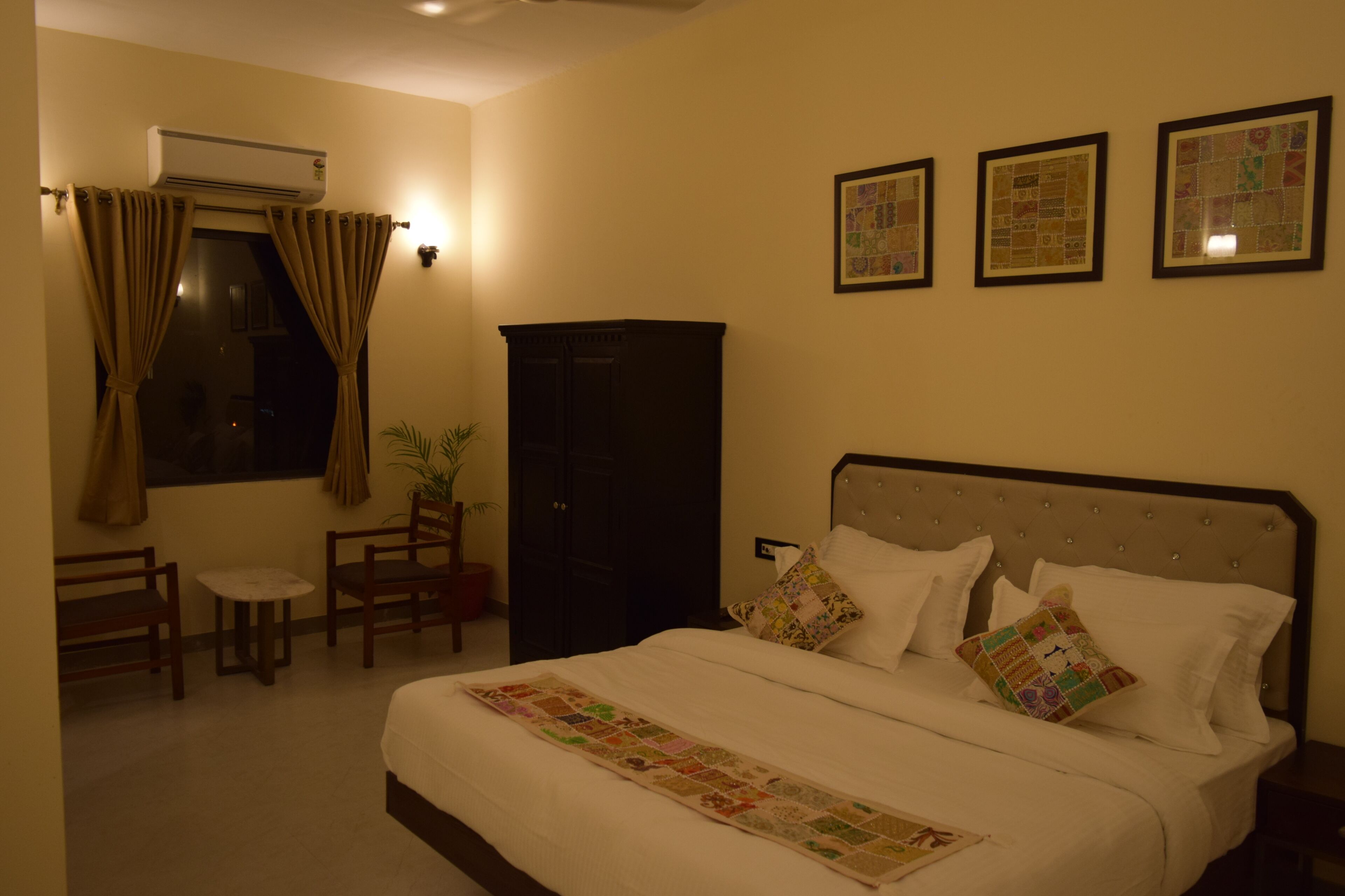 A bedroom with a bed, a desk, chairs, a wardrobe, and three framed pictures on the wall.