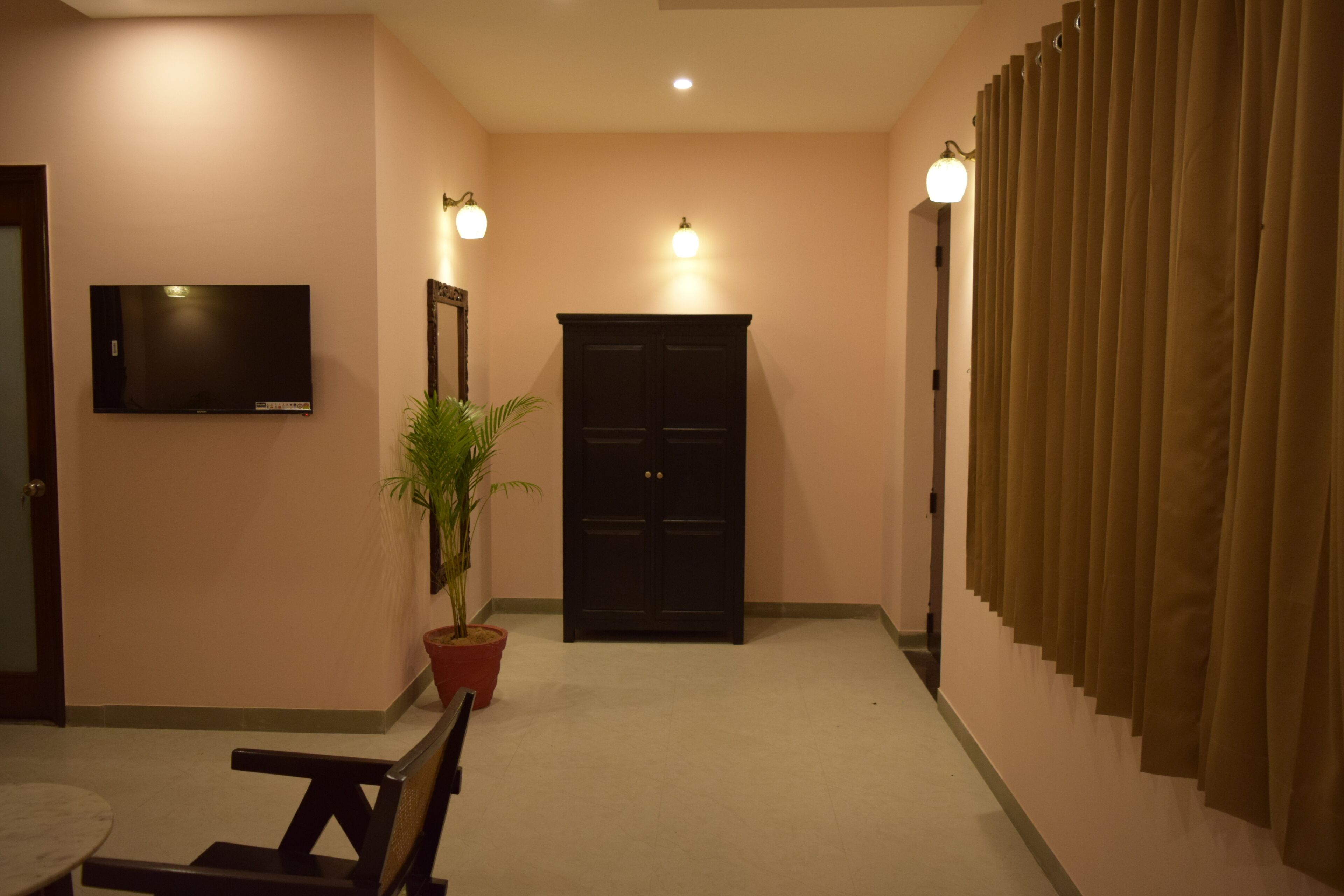 A hallway with a flat-screen TV mounted on the wall, a potted plant, a dark wooden door, and a curtain-covered window.
