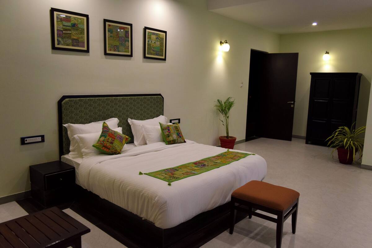 A neatly made bed with a green headboard, white bedding, and colorful pillows. There are three framed artworks on the wall above the bed.