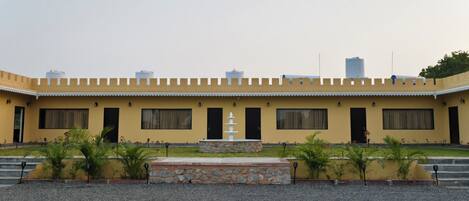 A building with a yellow facade, multiple windows, a central fountain, and a gravel courtyard.