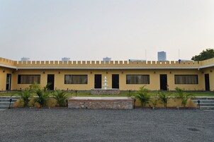 Un edificio con fachada amarilla, múltiples ventanas, una fuente central y un patio de grava.