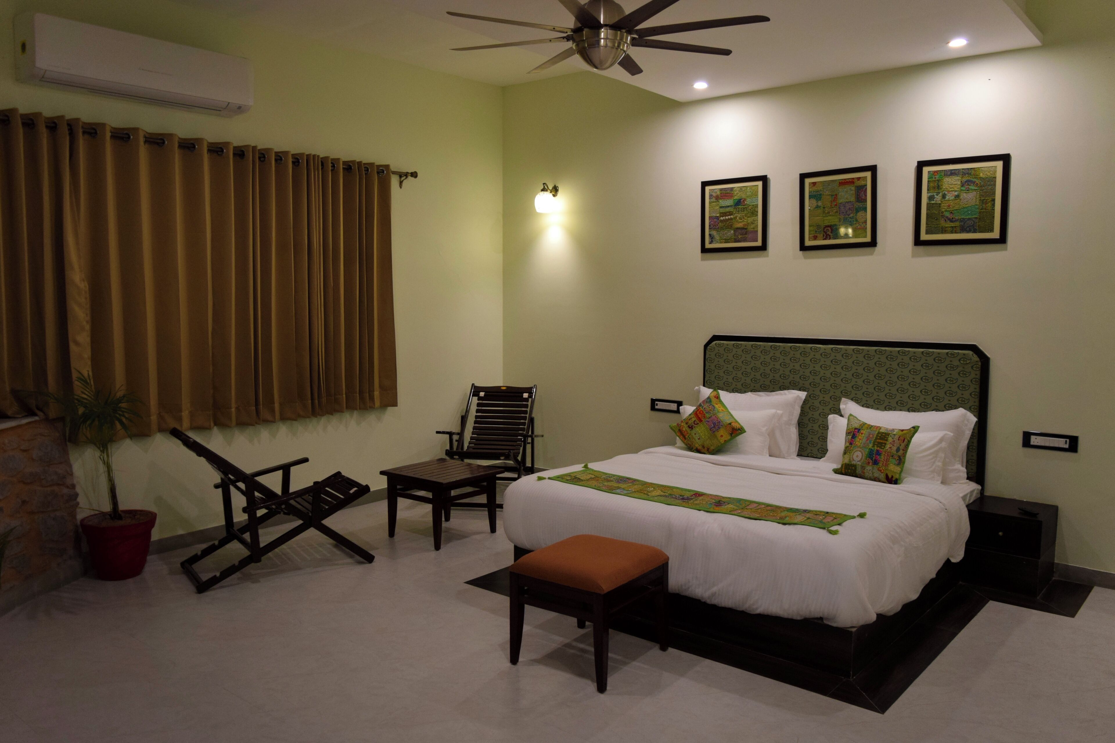 A hotel room with a bed, a chair, a small table, a potted plant, and a ceiling fan.