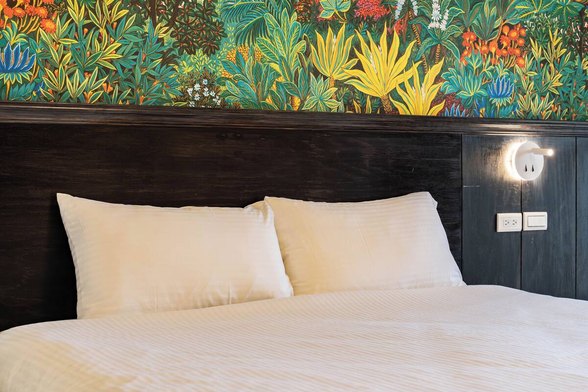 A bed with white bedding, a dark headboard, and a wall with a colorful botanical mural.