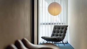 A modern interior with a tufted leather chair, a hanging paper lantern, and a view through sheer curtains. - yunhua bib (Hualien City)