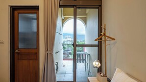 A hotel room with a bed, a bedside table with a lamp, a wooden hanger, and a view of the outside balcony with chairs and a railing. - yunhua bib (Hualien City)