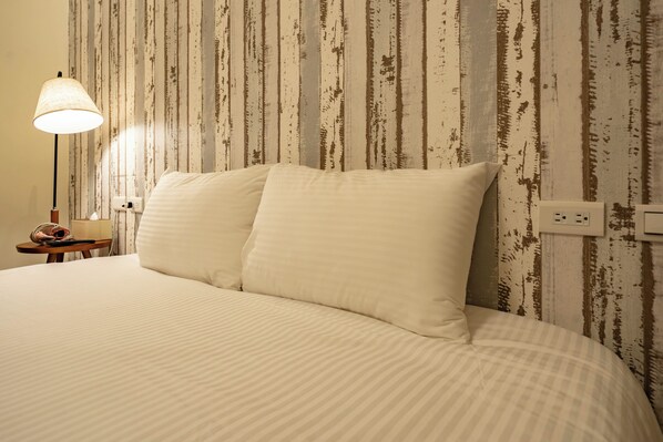 A neatly made bed with a striped bedspread and two pillows, a bedside lamp, and a wall with vertical wooden planks. - yunhua bib (Hualien City)