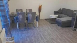 A living room with a grey sofa, a round coffee table, and two armchairs. There is a broom and a small table with a vase on the floor. - Family House (Beauvais)