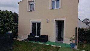 A two-story building with a flat roof, a green lawn, and a small patio area with outdoor furniture. - Family House (Beauvais)