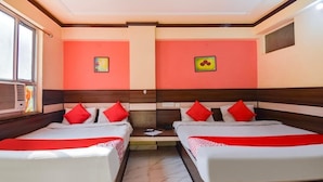 A hotel room with two beds, red and white bedding, a window with blinds, and a wall-mounted air conditioning unit. - Hotel Churu Palace (Jaipur)