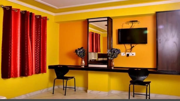 A room with yellow walls, a black desk, two black chairs, a mirror, a television, and a wardrobe. - Hotel Churu Palace (Jaipur)