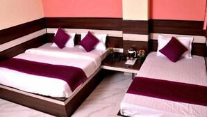 A hotel room with two beds, each with a wooden headboard, white bedding, and purple pillows. A small table with a coffee maker and flowers is between the beds. - Hotel Churu Palace (Jaipur)