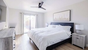 Une chambre à coucher moderne, avec un lit, des tables de chevet, un ventilateur de plafond et une grande fenêtre avec des rideaux.