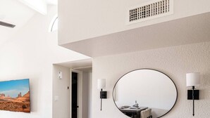 Une chambre d’hôtel moderne dotée d’un coin repas, d’un grand miroir rond et offrant une vue sur un paysage désertique.