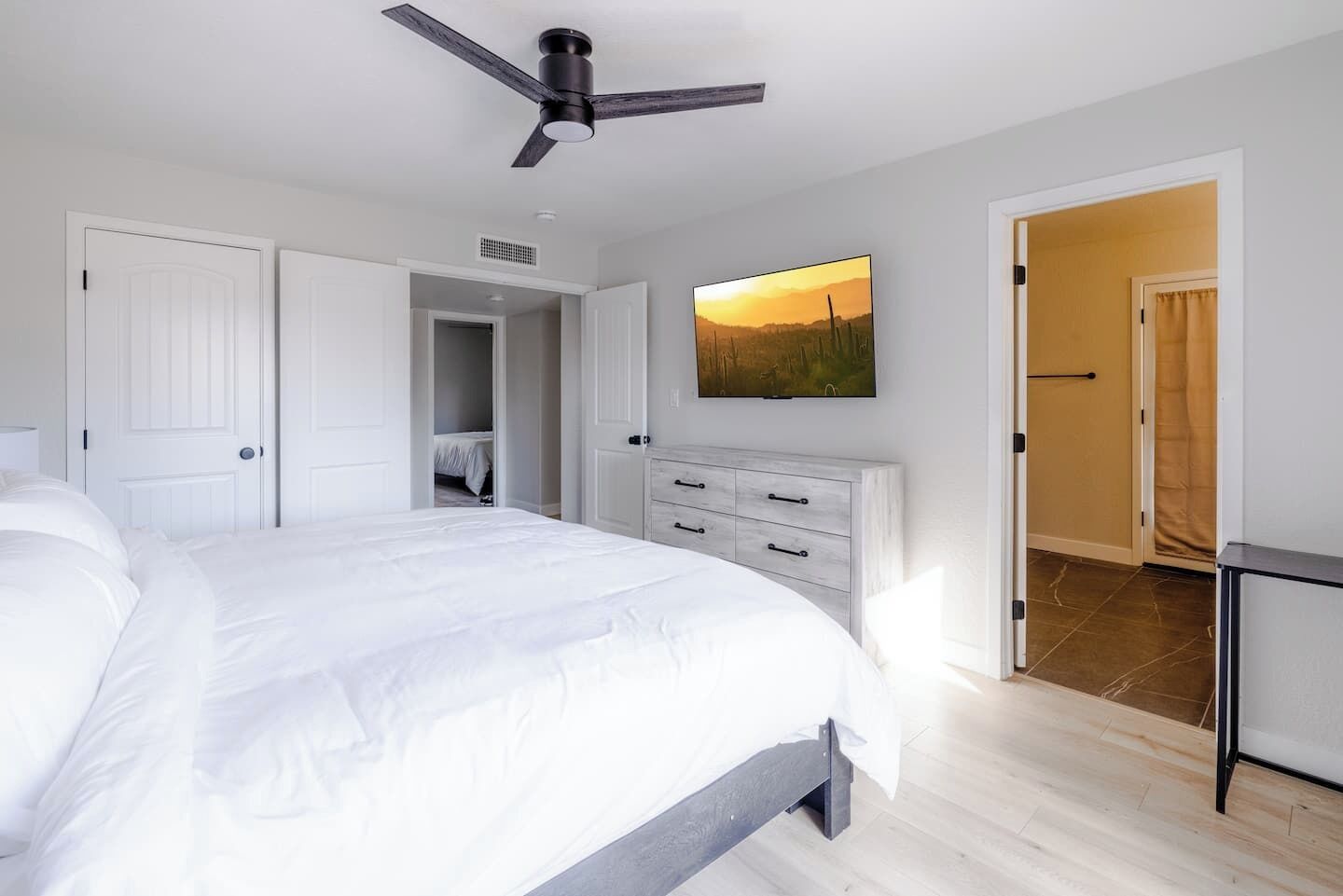 Een slaapkamer met een bed, een dressoir, een plafondventilator en een schilderij aan de muur.