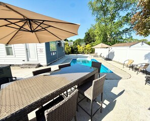 Un patio trasero con piscina, mobiliario exterior y un área de patio techada.