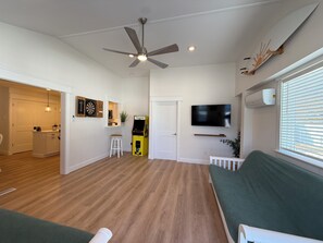 Un espace de vie compact doté d’un ventilateur de plafond, d’un téléviseur à écran plat, d’un jeu de fléchettes et d’une petite kitchenette.