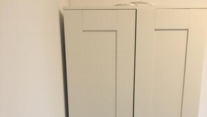 A white wardrobe with two doors and a handle, located next to a bed in a room. - Hallera Wroclaw (Wrocław)