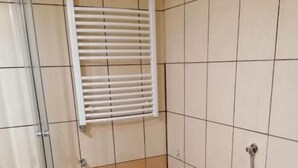 A small bathroom with a toilet, a shower, and a window with blinds. - Hallera Wroclaw (Wrocław)