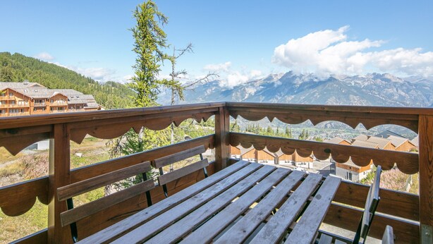 A wooden deck with a bench overlooking a mountainous landscape with buildings in the background. - Snug Apartment on the Mountains (Risoul)