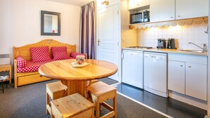 A cozy room with a wooden bed, a dining table, and a kitchen area with white cabinets and appliances. - Snug Apartment on the Mountains (Risoul)