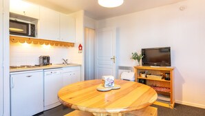 A compact kitchen with white cabinets, a microwave, a coffee maker, and a television on a wooden stand. - Snug Apartment on the Mountains (Risoul)