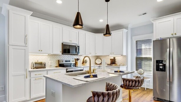 Een moderne keuken met witte kasten, een centraal eiland, roestvrijstalen apparatuur en twee barkrukken met gouden details.