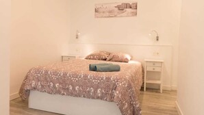 A bedroom with a bed, a bedside table, a nightstand, a wall-mounted picture, and a window with curtains.