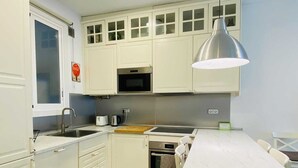 A compact kitchen with white cabinets, a stainless steel sink, a microwave, and a table with chairs.