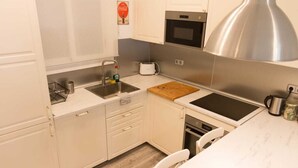 A compact kitchen with a sink, stove, oven, and a cutting board on the countertop.