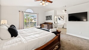 A bedroom with a large bed, a ceiling fan, a TV, and a view of the outdoors. - Casa Bella Gardens- Spacious 5-bedroom house in welcoming Bakersfield with Pool (Bakersfield)