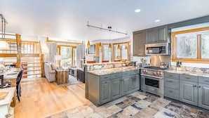 A modern kitchen with grey cabinets, a large island, and a dining area with a staircase. - Tomboy Townhome-Curate Telluride, Near Market, Walk to Ski, Town, Modern (Telluride)