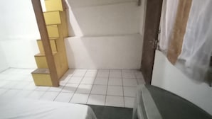 A small, tiled room with a bed, a wooden staircase, and a door. - OYO 94801 Pad Guest House (Bandung)
