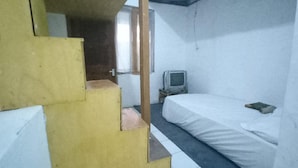 A small, compact room with a single bed, a television on a small table, and a door leading to another room. - OYO 94801 Pad Guest House (Bandung)