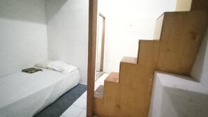 A room with a single bed, a small table, and a wooden staircase. - OYO 94801 Pad Guest House (Bandung)
