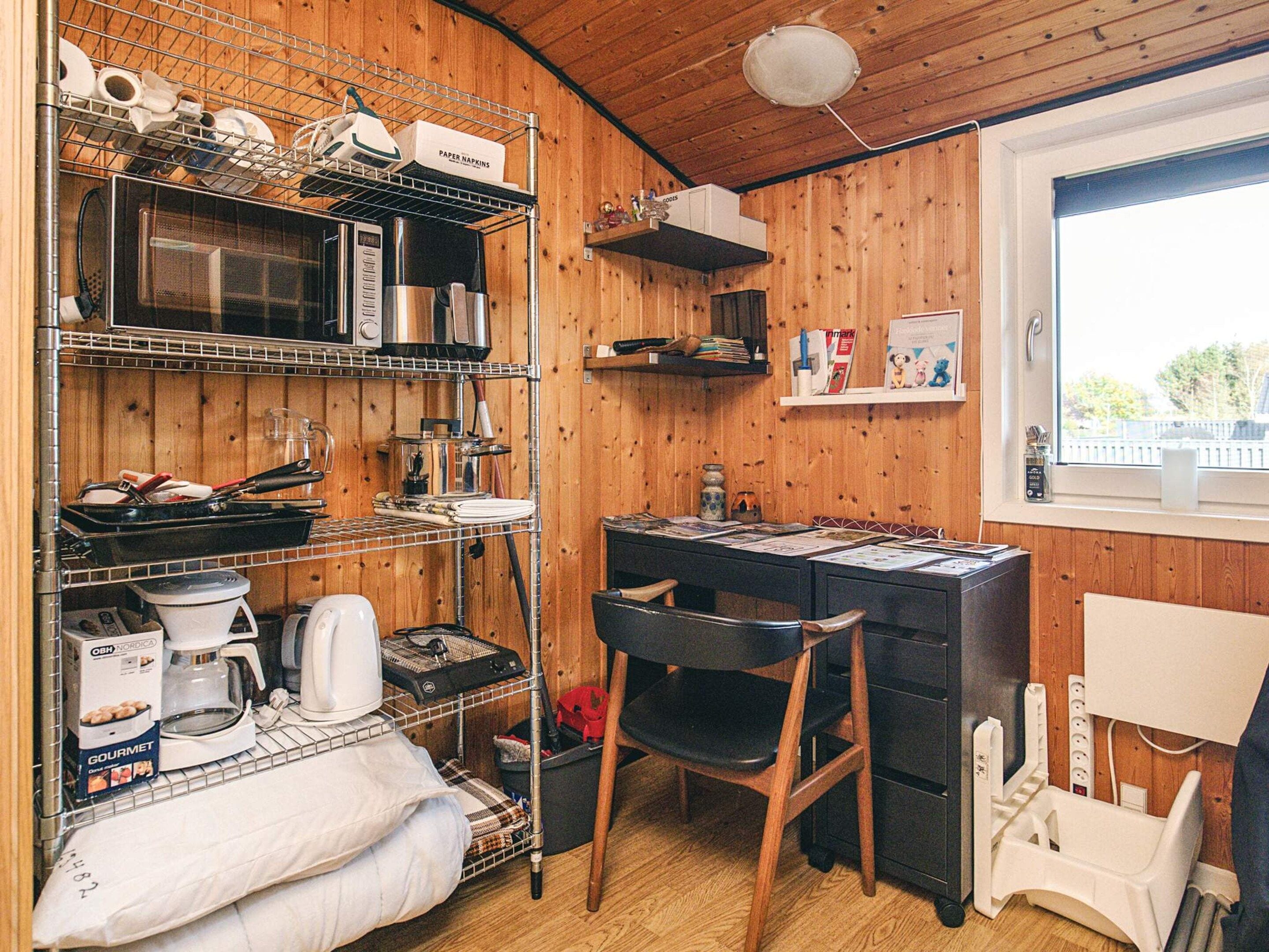A kitchen with wooden walls, a microwave, a coffee maker, and a shelf with paper napkins.